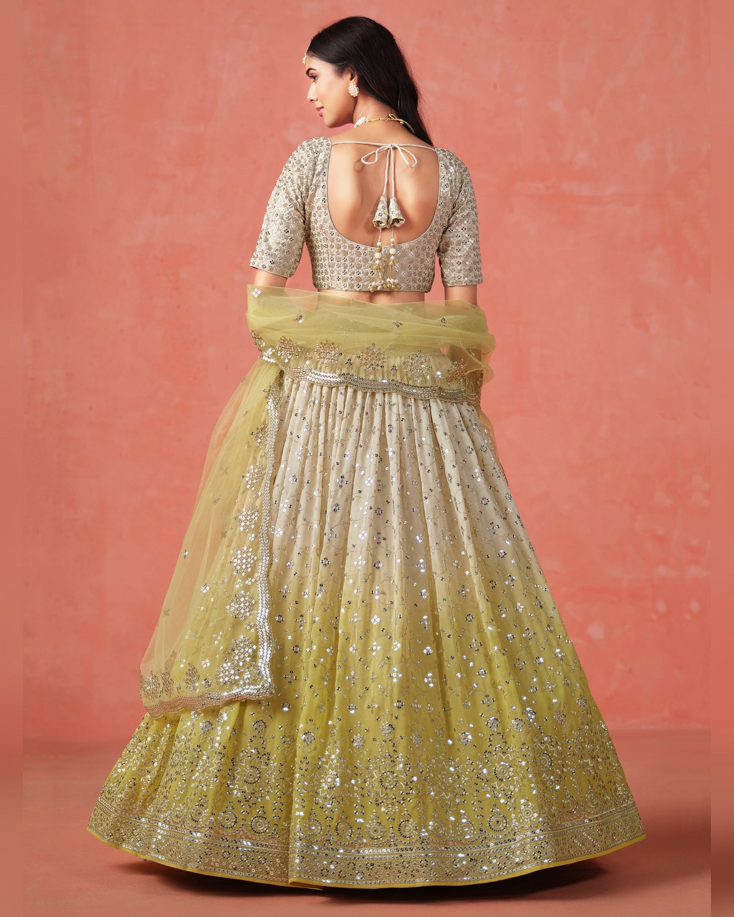Woman wearing a traditional outfit with a yellow and silver lehenga against a pink background