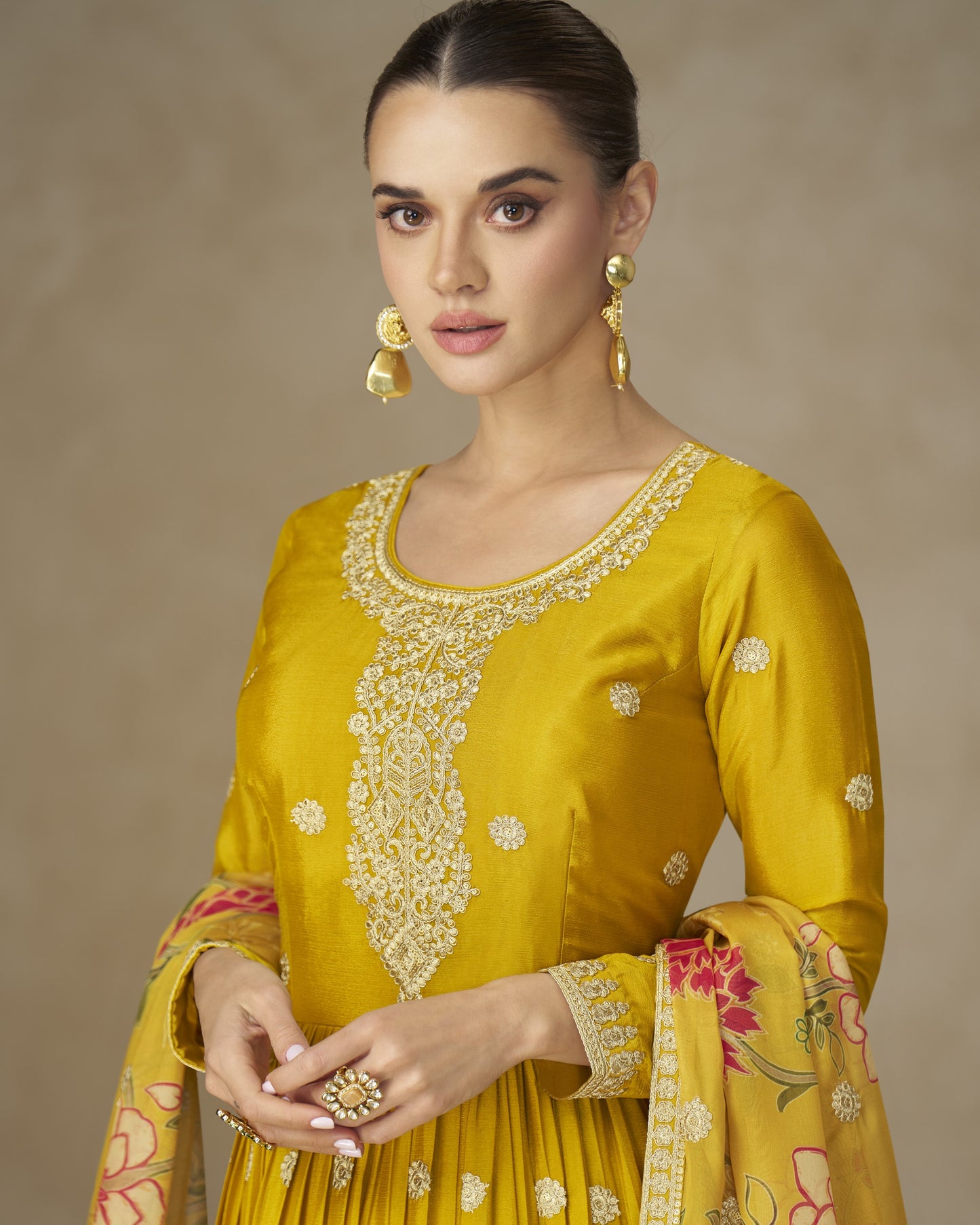 Woman wearing a yellow embroidered traditional outfit with a plain background