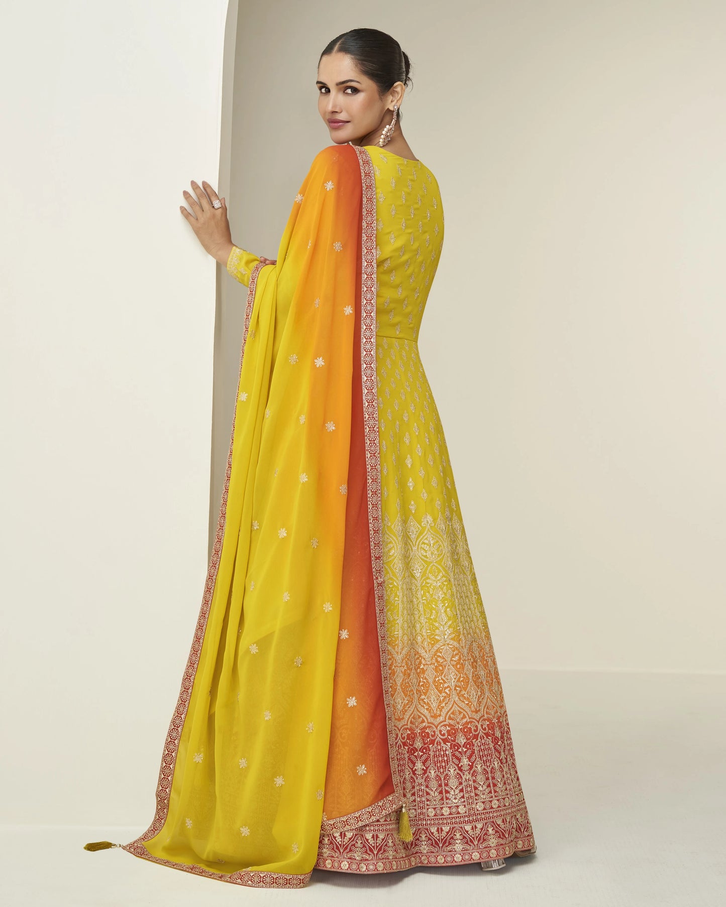 Woman wearing a yellow and orange saree with a plain background