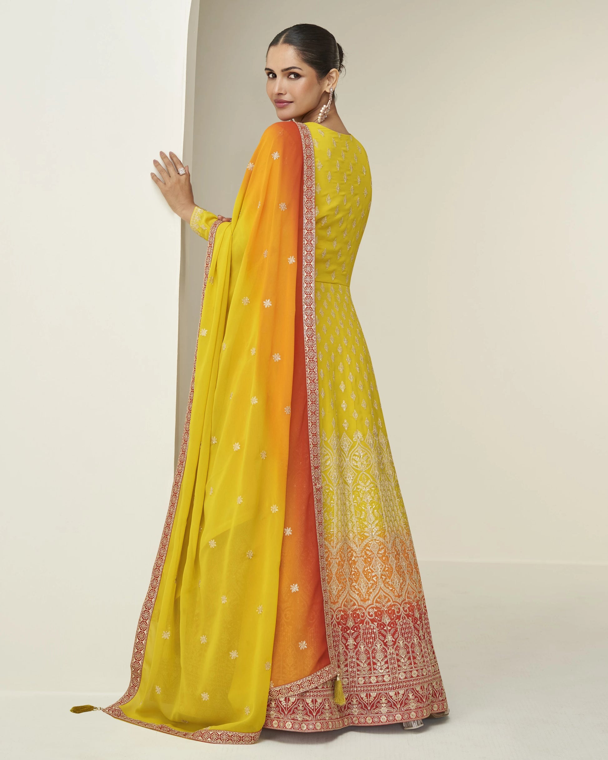 Woman wearing a yellow and orange saree with a plain background