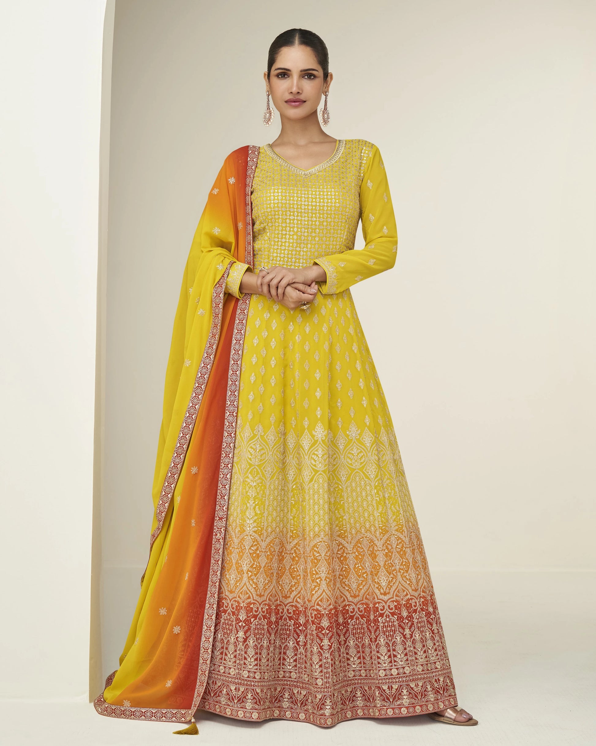 Woman wearing a yellow and orange traditional outfit with a matching dupatta on a plain background