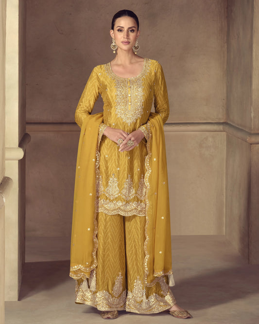 Woman wearing a mustard yellow embroidered traditional outfit with a plain background