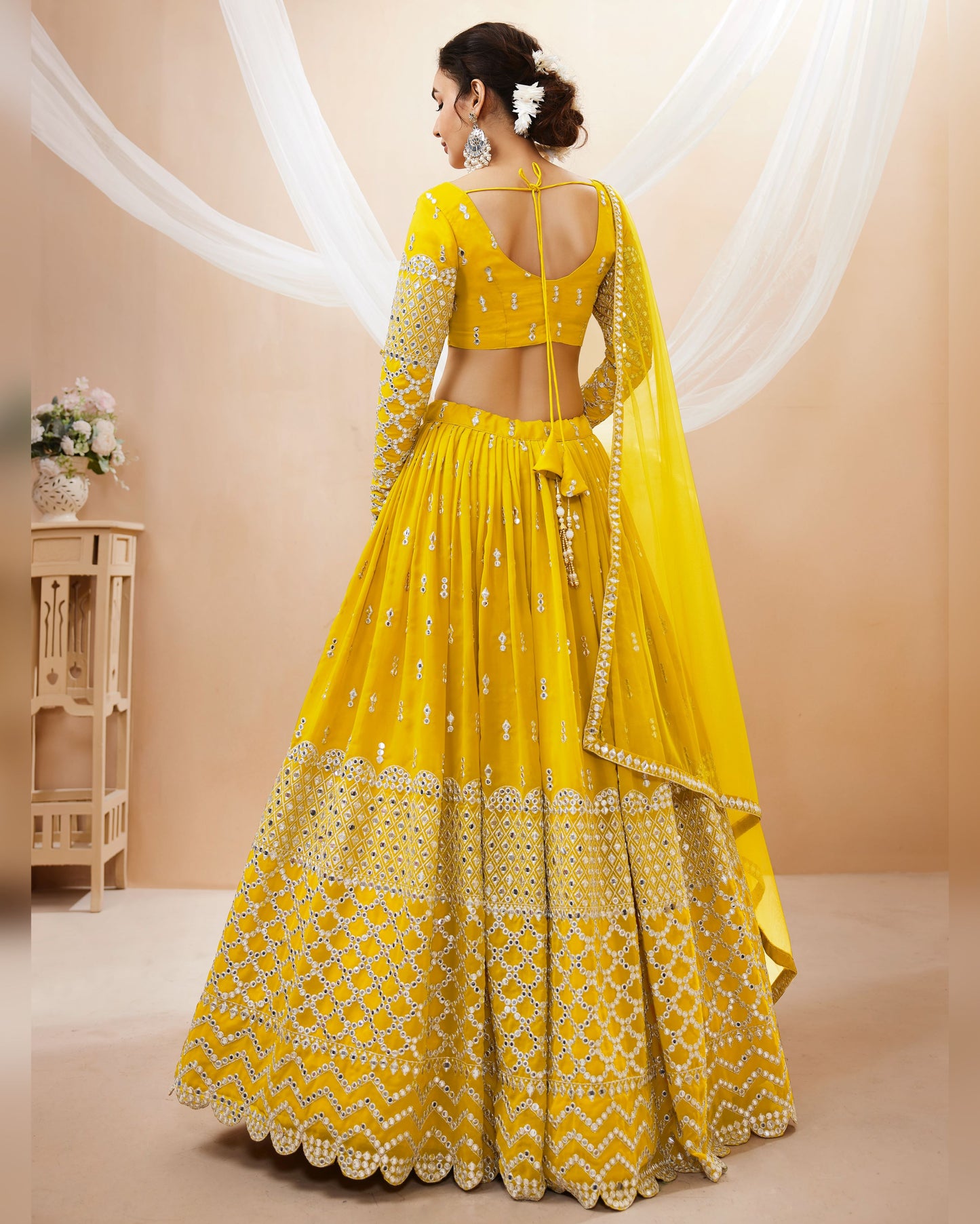 Woman wearing a yellow traditional outfit with a matching dupatta against a beige background