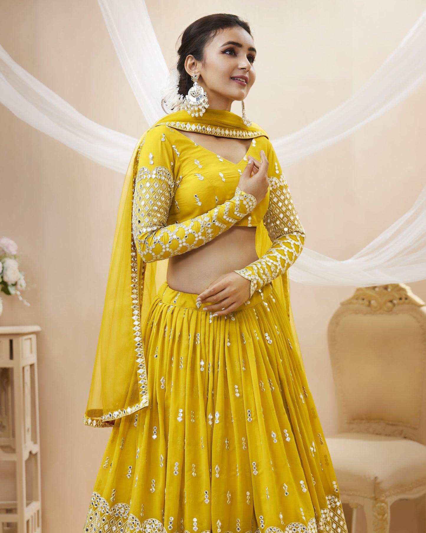 Woman wearing a yellow traditional outfit with white patterns in a decorated room.