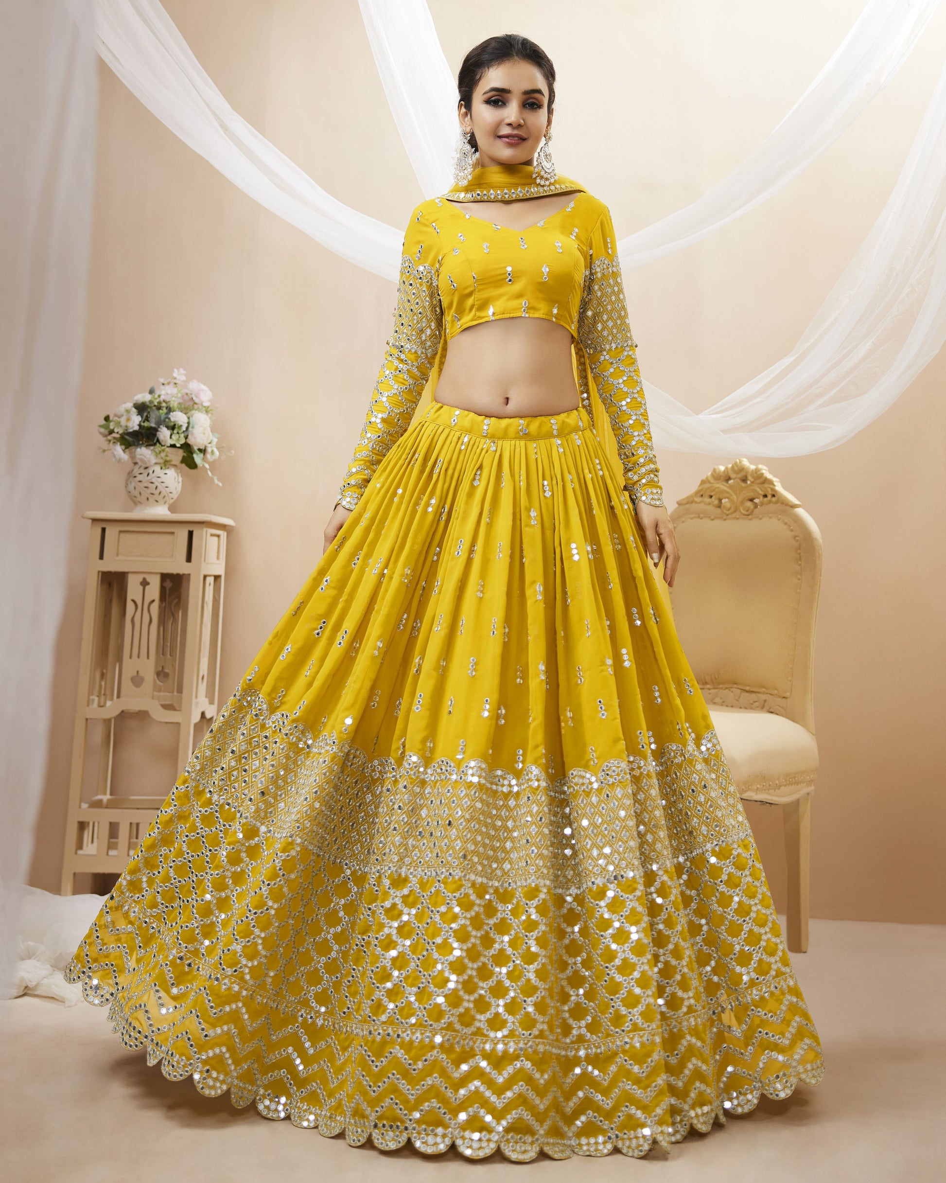 Woman wearing a yellow embroidered lehenga in a decorated room.