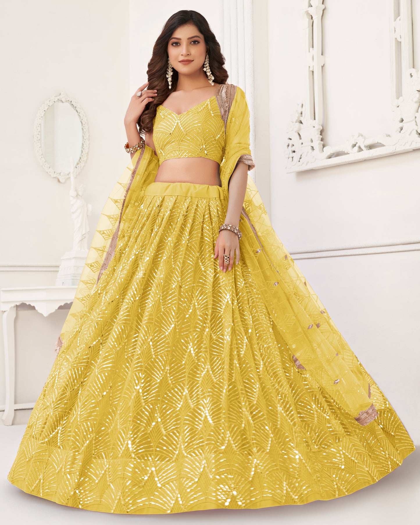 Woman wearing a yellow traditional outfit with intricate patterns in a white room.