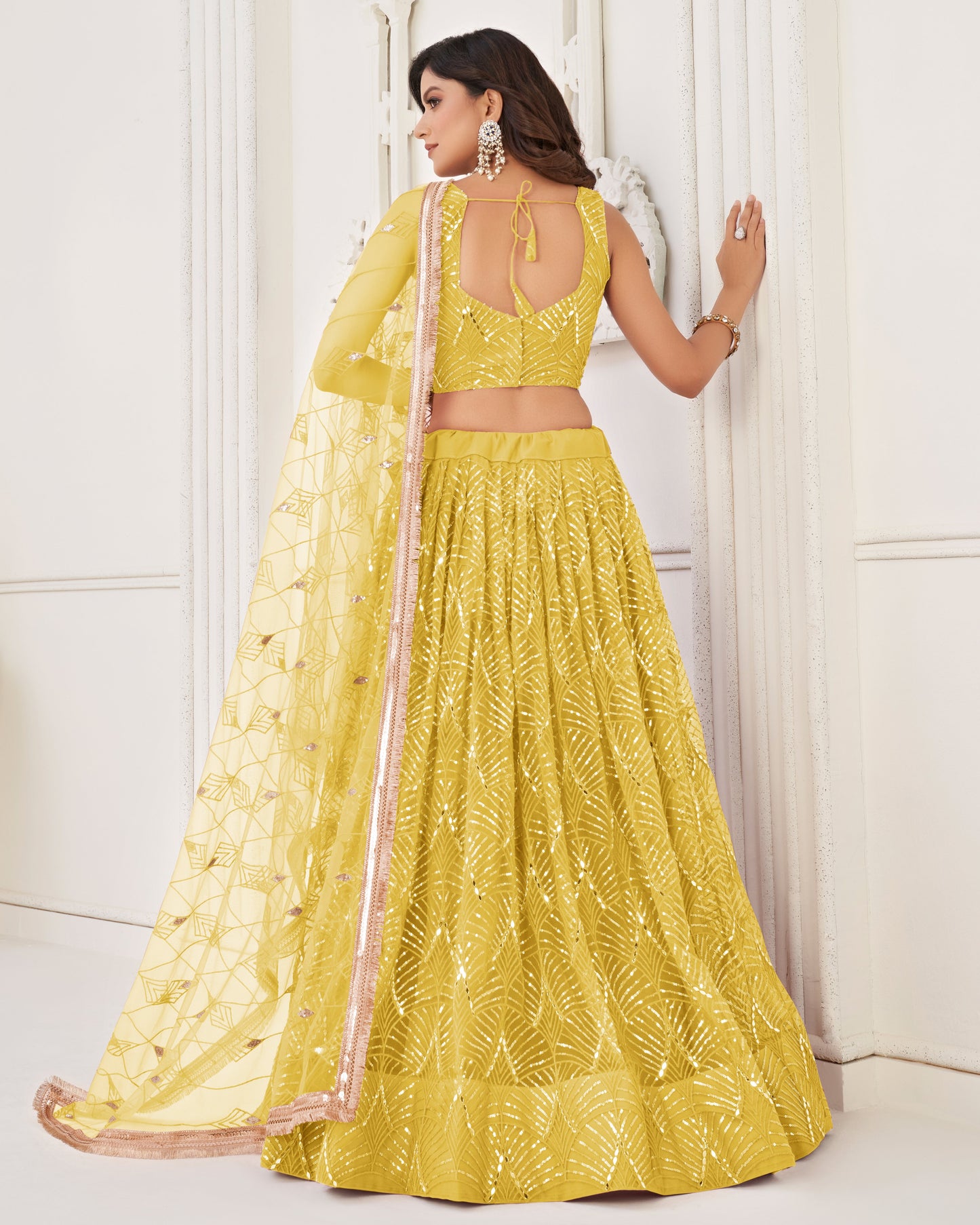 Woman wearing a yellow embroidered lehenga with a white background