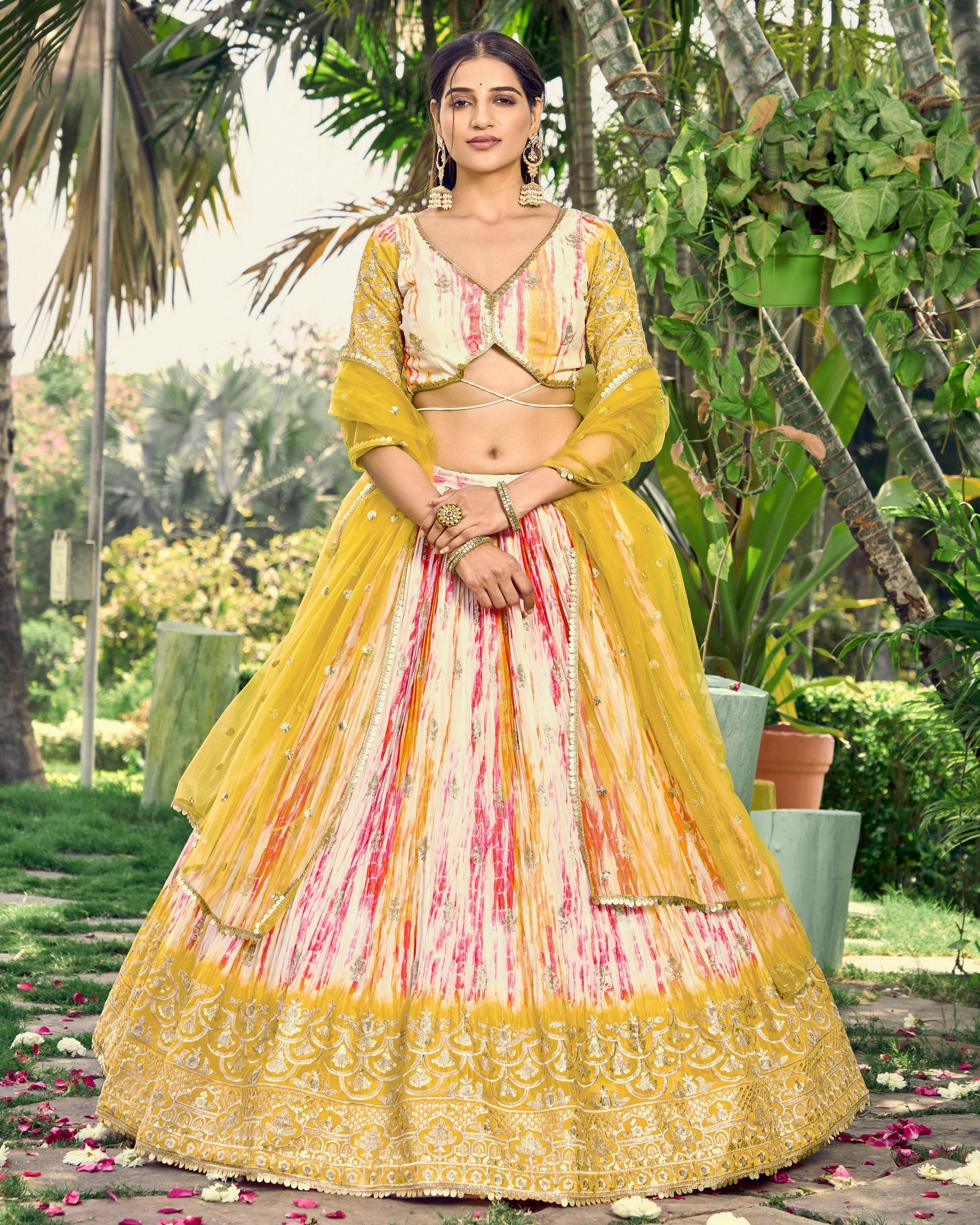 Woman in a yellow and pink traditional outfit standing outdoors with greenery in the background