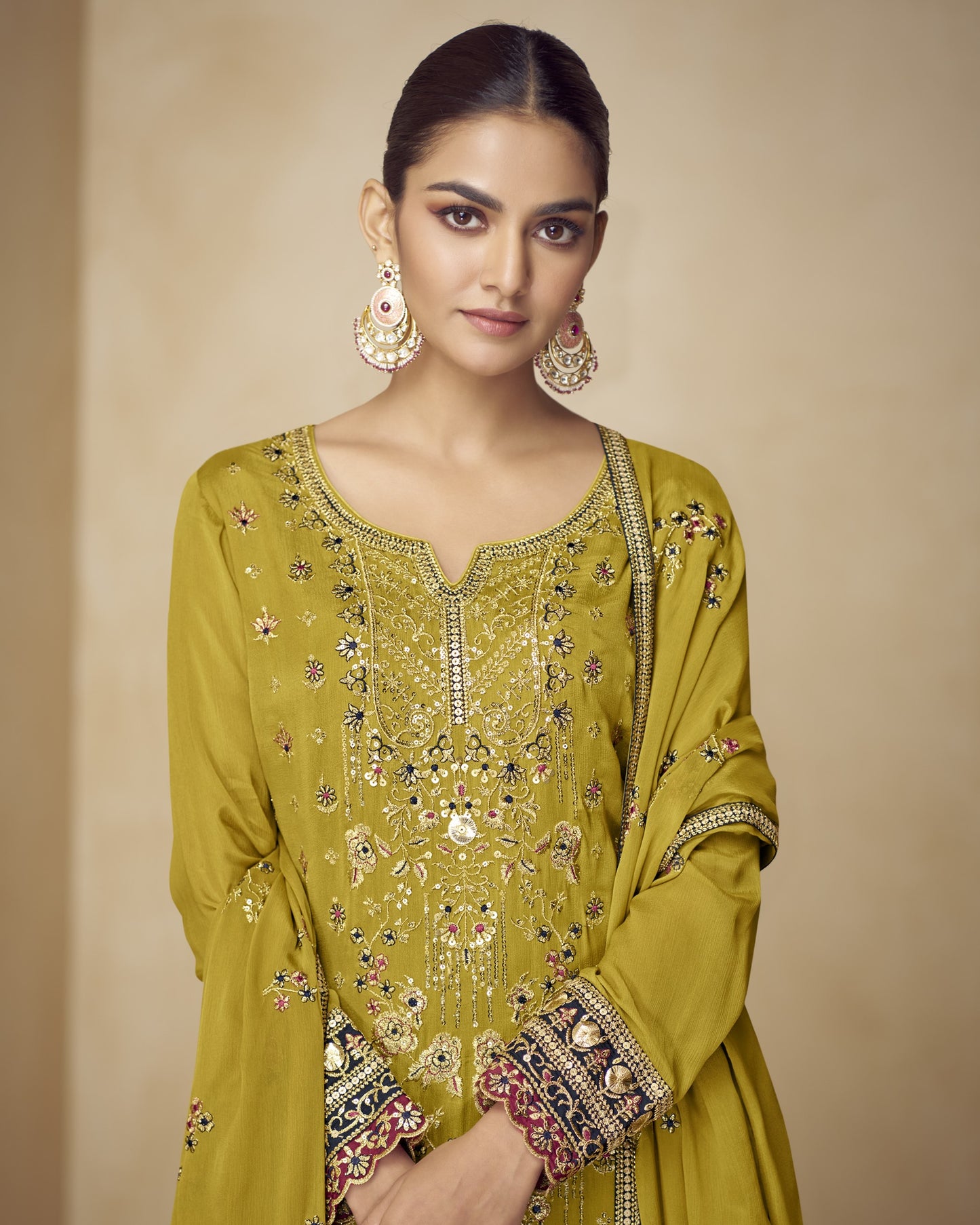 Woman wearing a green embroidered traditional outfit with gold jewelry on a beige background