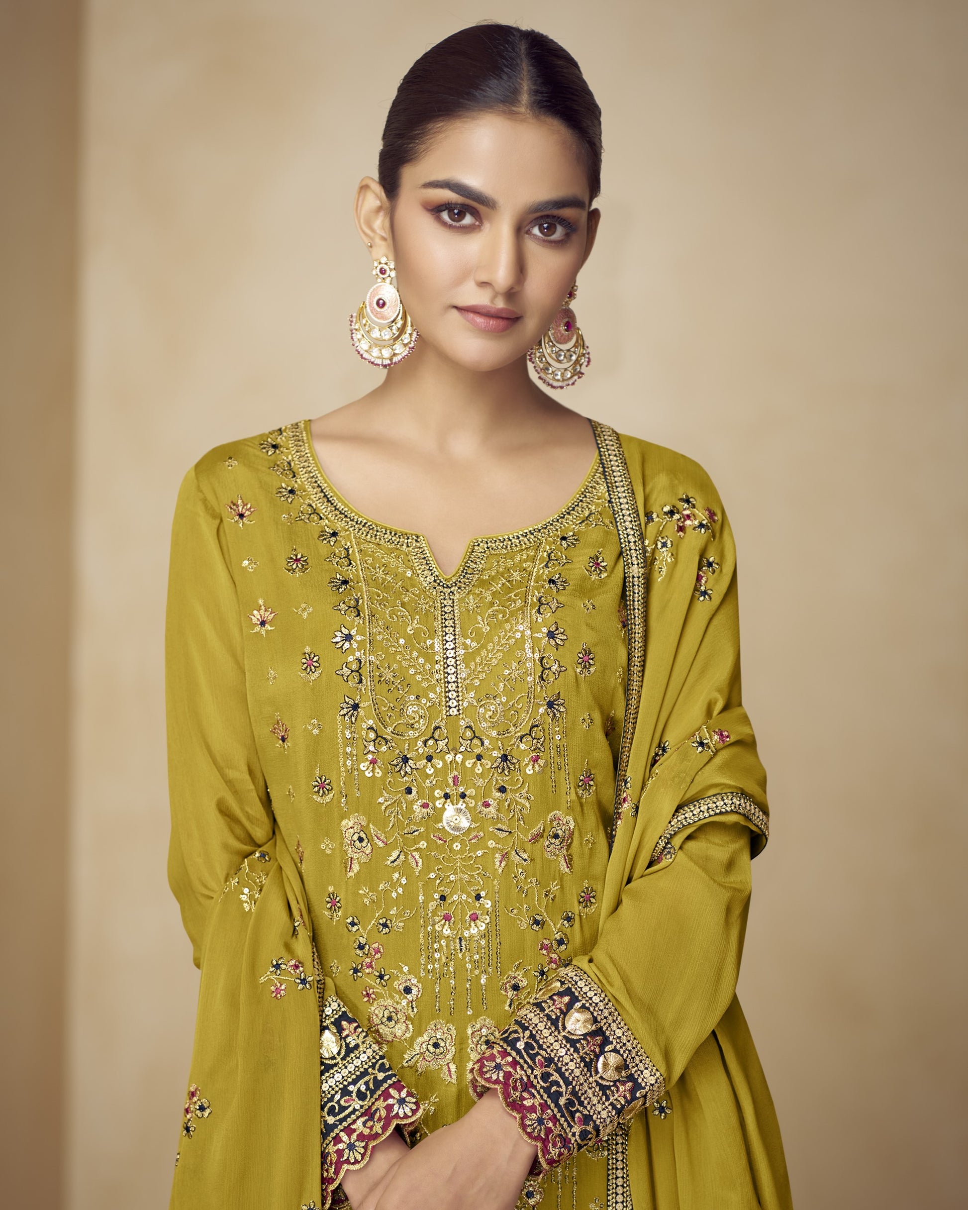 Woman wearing a green embroidered traditional outfit with gold jewelry on a beige background