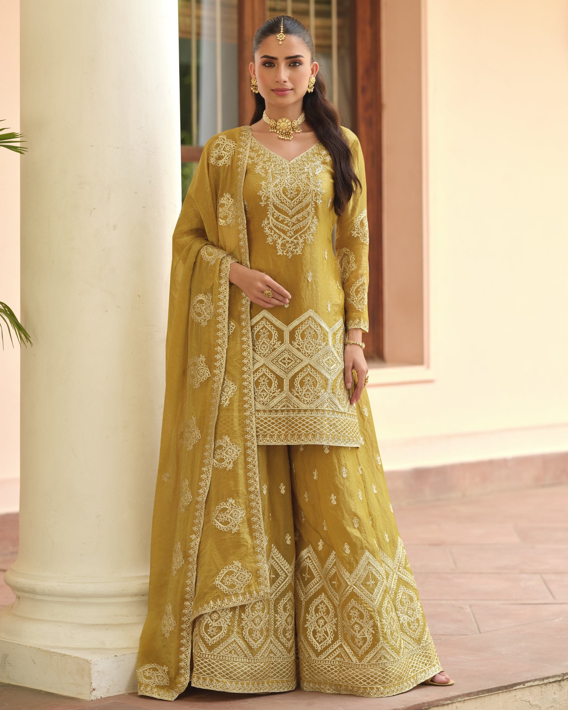 Woman wearing a yellow embroidered traditional outfit standing in front of a building.