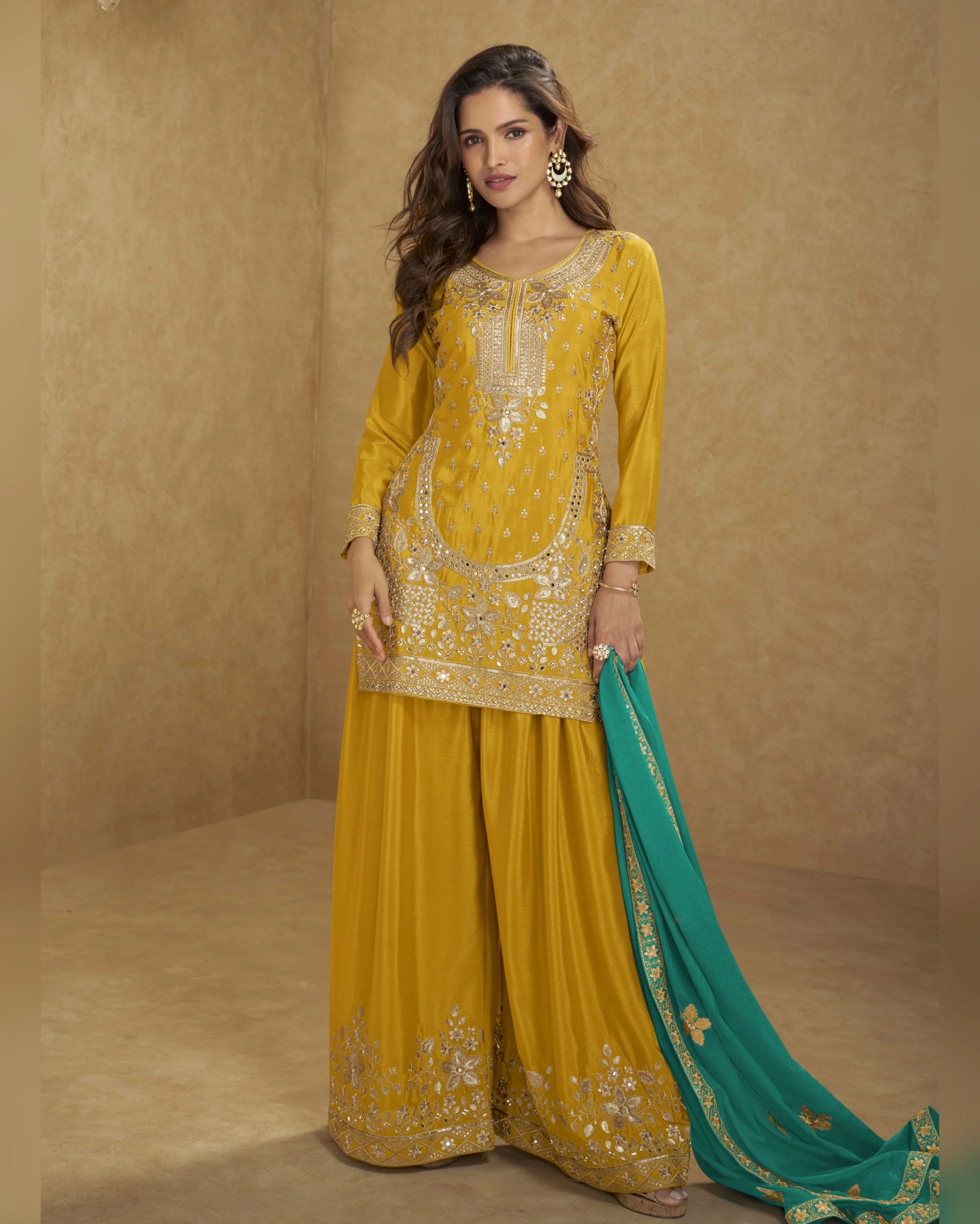 Woman wearing a yellow embroidered outfit with a green dupatta against a beige background