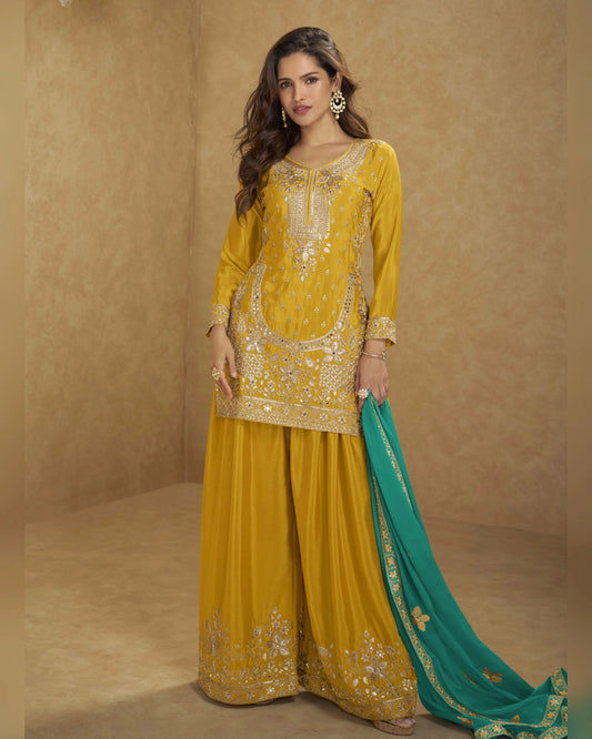 Woman wearing a yellow embroidered outfit with a green dupatta against a beige background