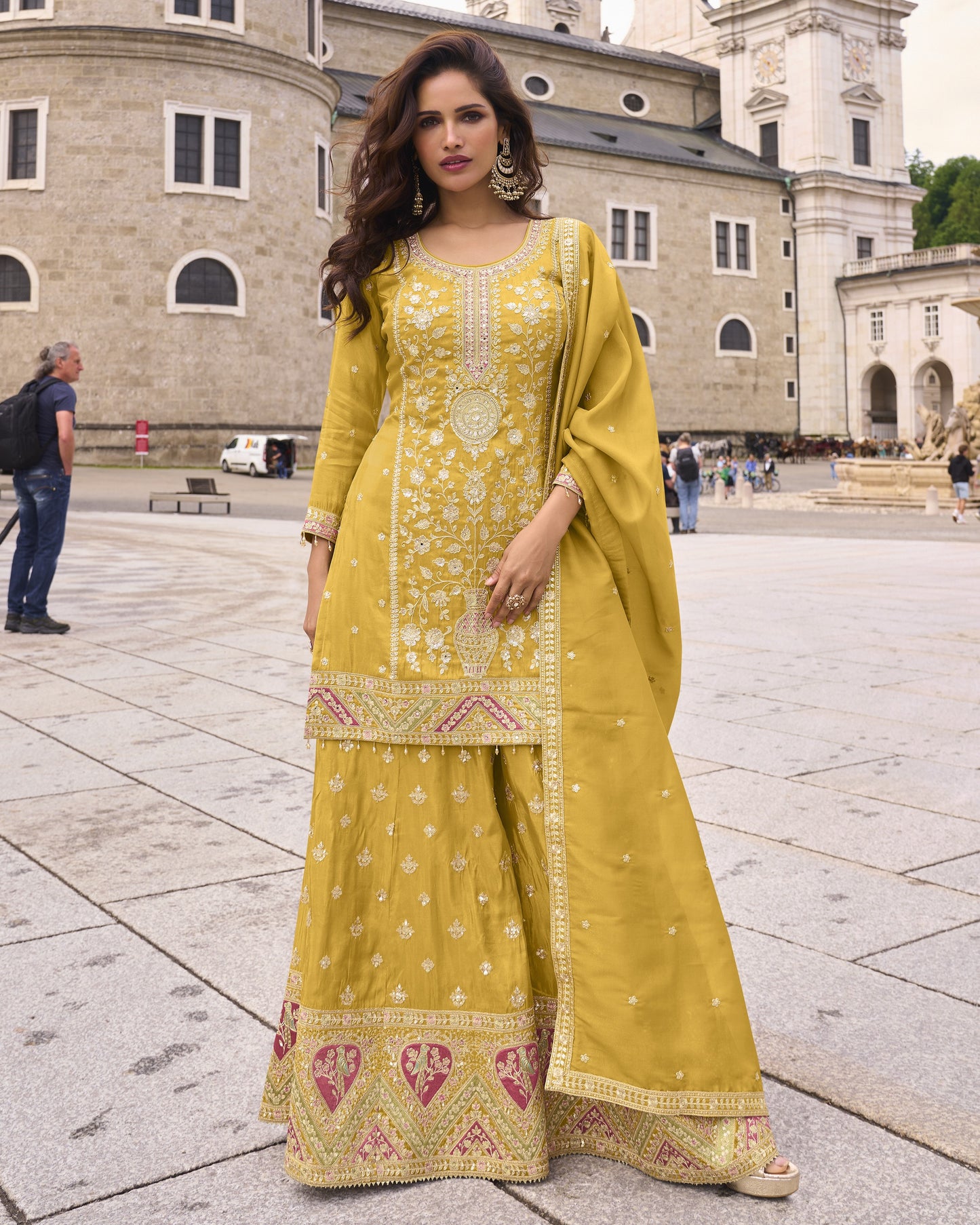 Woman in a yellow traditional outfit standing in an outdoor setting with architectural background