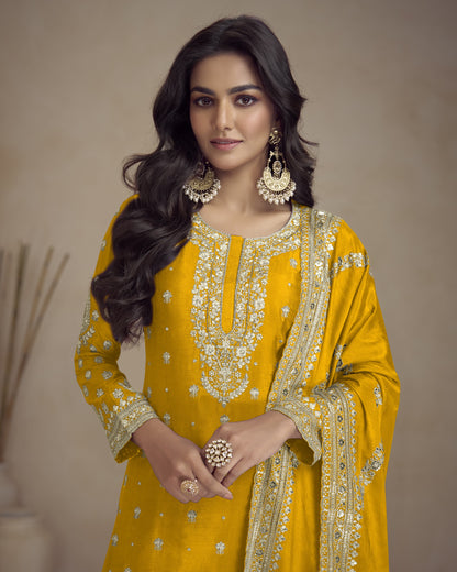 Woman wearing a yellow embroidered traditional outfit with gold jewelry against a neutral background