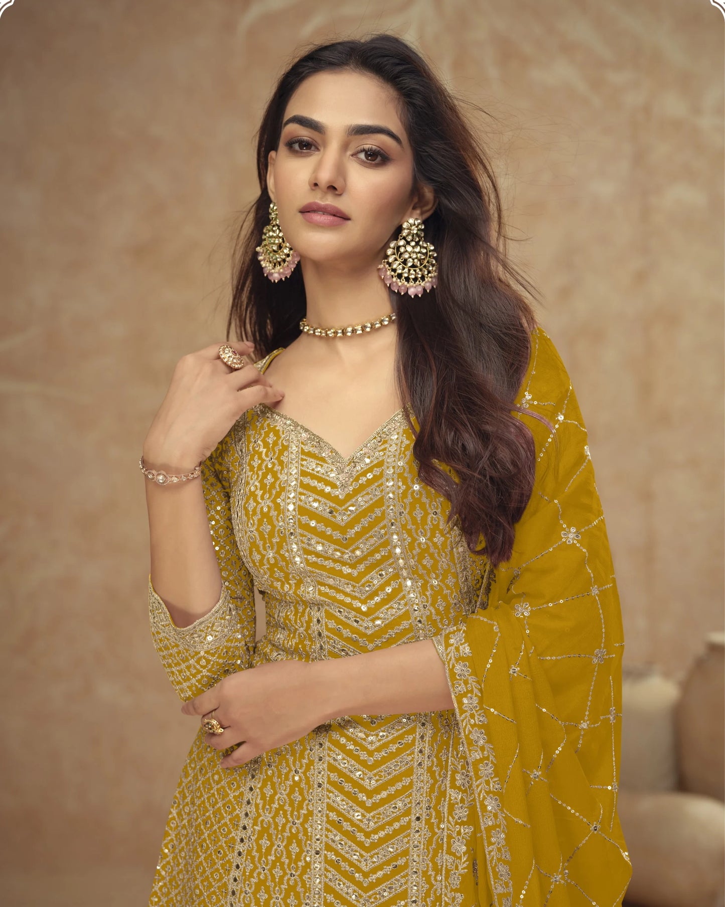 Woman in a yellow traditional outfit with gold jewelry against a beige background