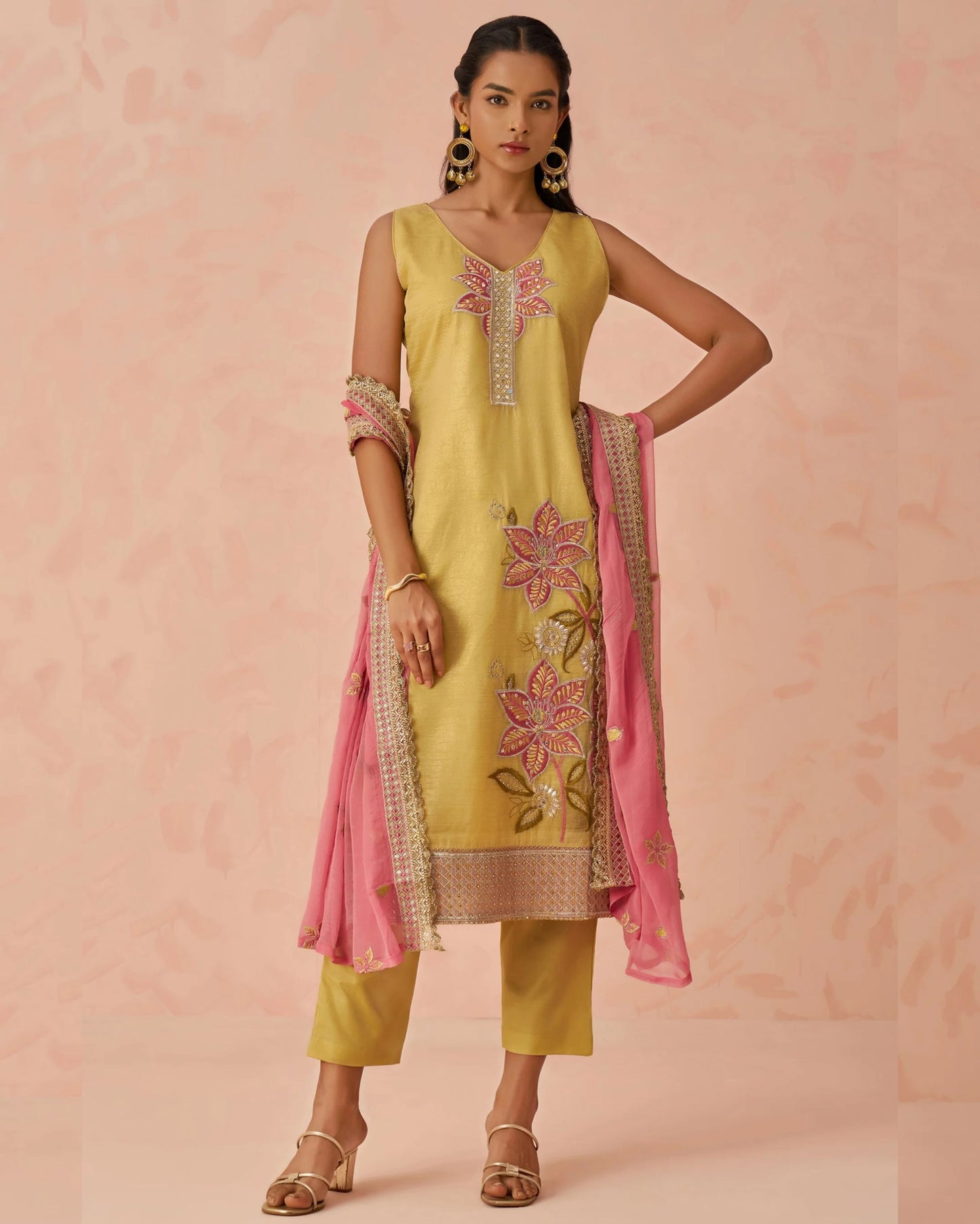 Woman wearing a yellow embroidered outfit with a pink dupatta on a pink background