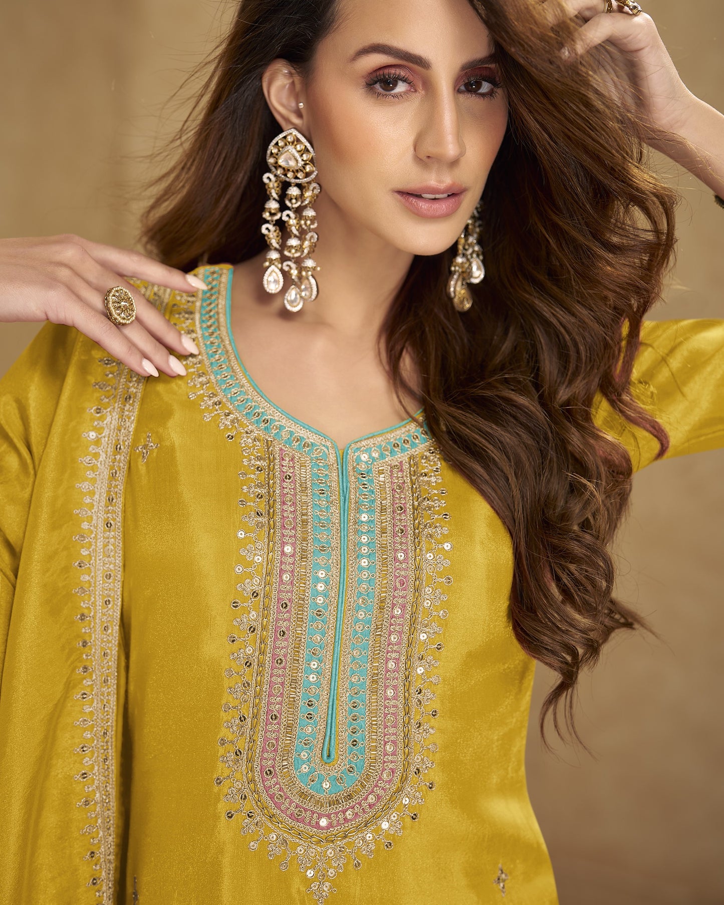 Woman wearing a yellow embroidered traditional outfit with gold jewelry against a beige background