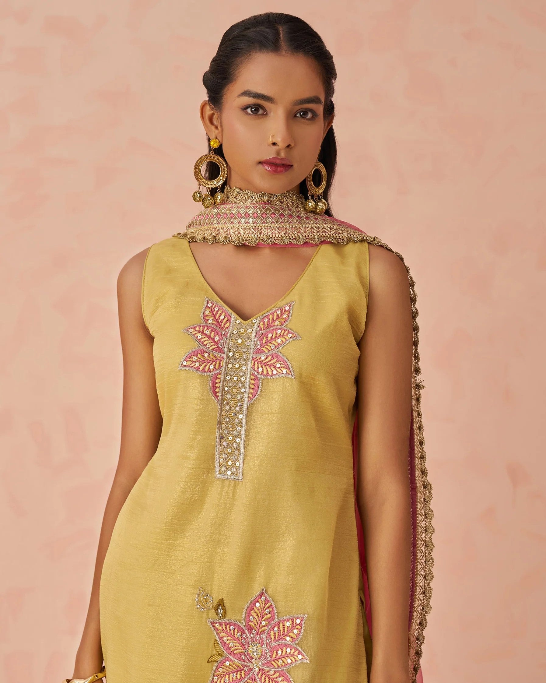 Woman wearing a yellow embroidered dress with a pink floral design on a pink background