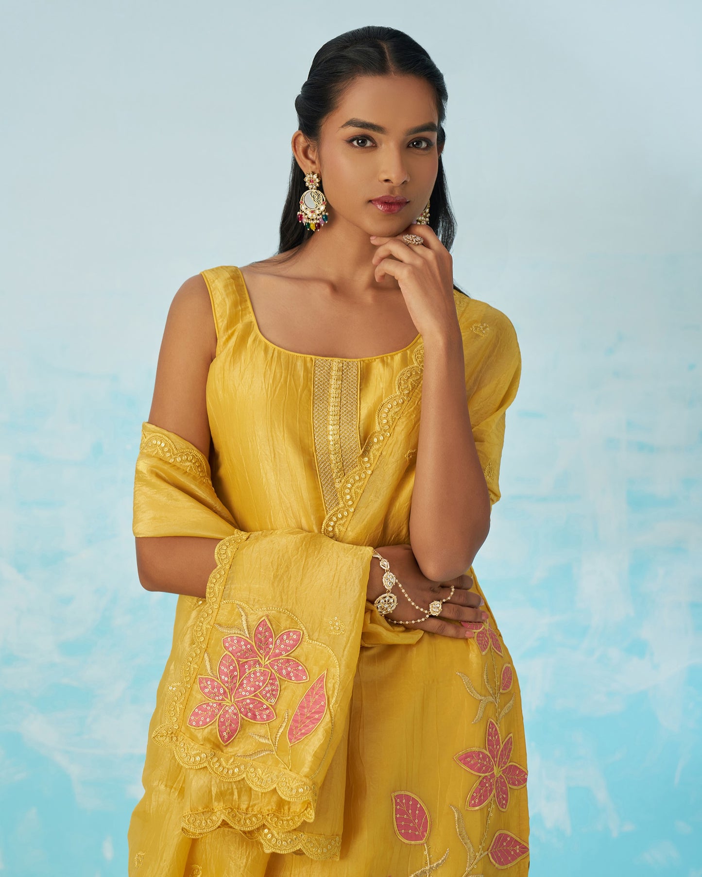 Woman wearing a yellow embroidered dress with pink floral patterns against a light blue background