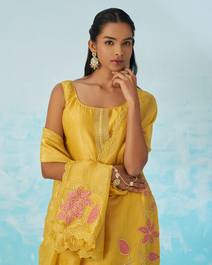 Woman wearing a yellow embroidered dress with pink floral patterns against a light blue background