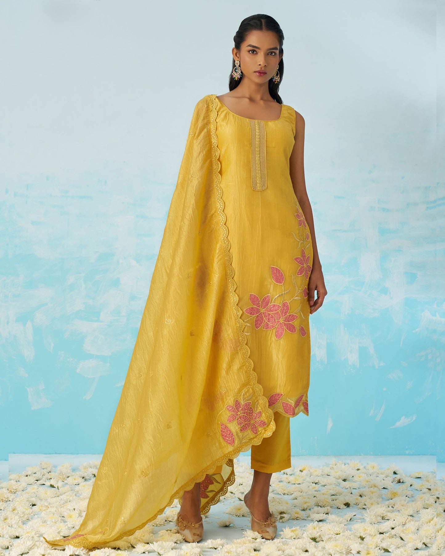 Woman wearing a yellow outfit with floral embroidery against a light blue background