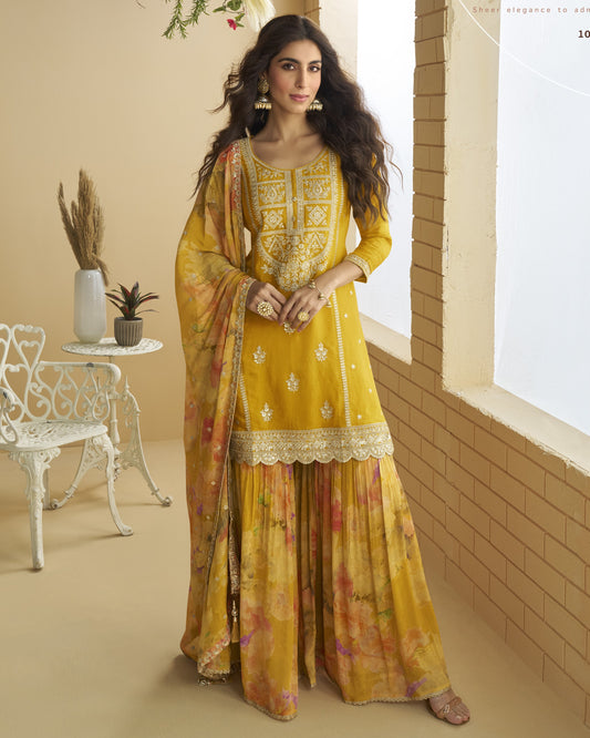 Woman in a yellow traditional outfit standing in a room with a white chair and small table.