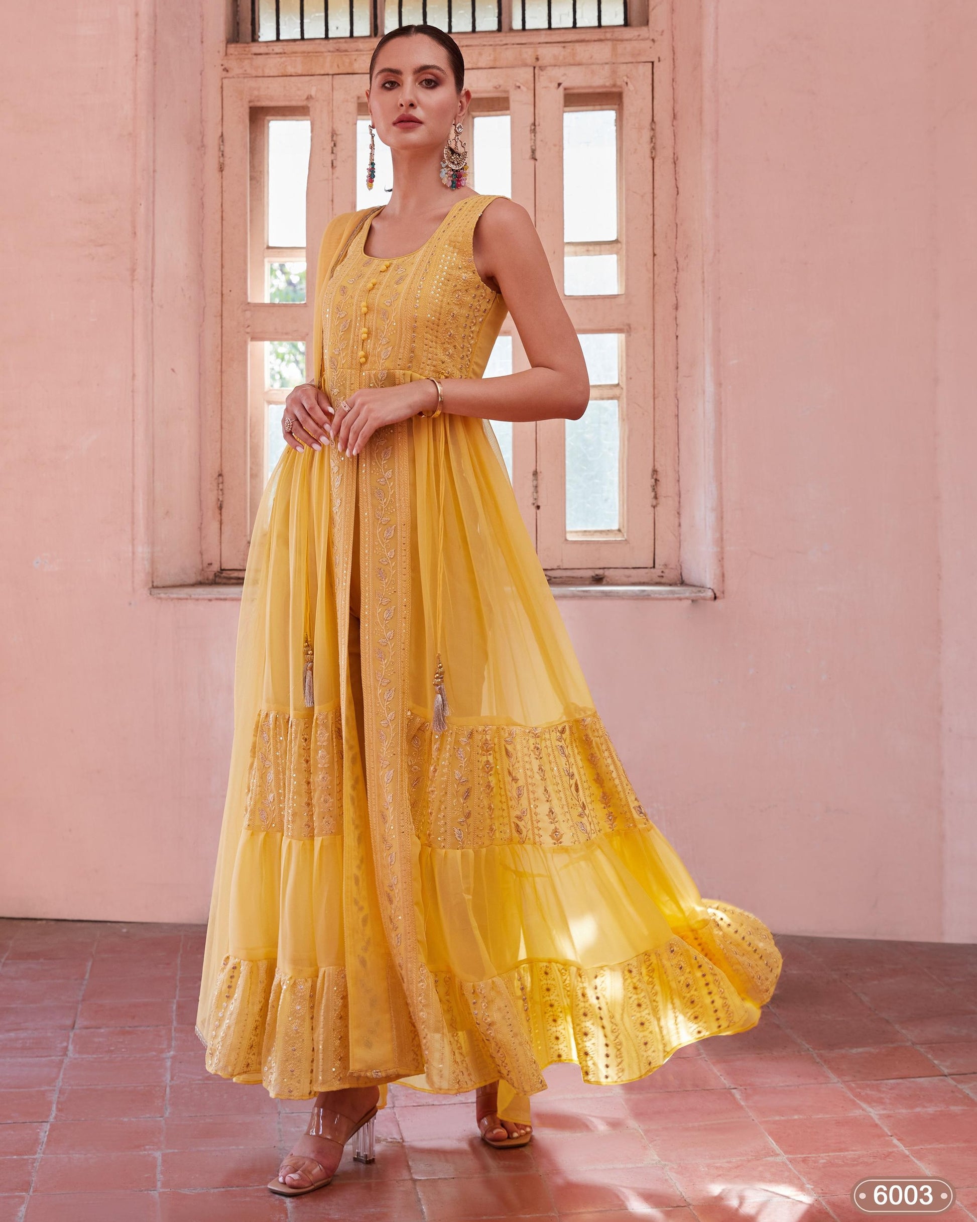 Woman wearing a yellow dress standing in a room with pink walls and wooden windows.