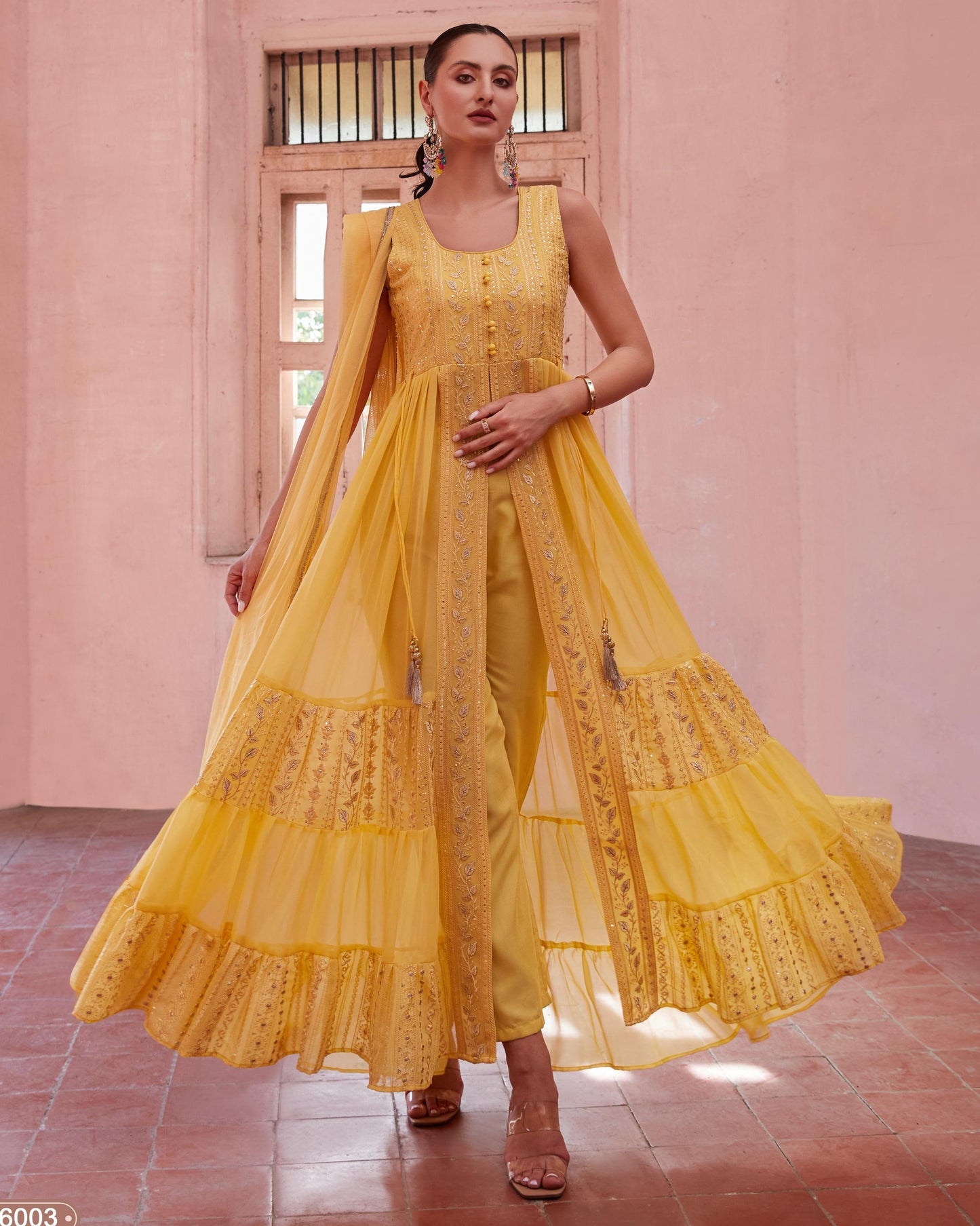 Woman wearing a yellow outfit with intricate designs in a pink room.