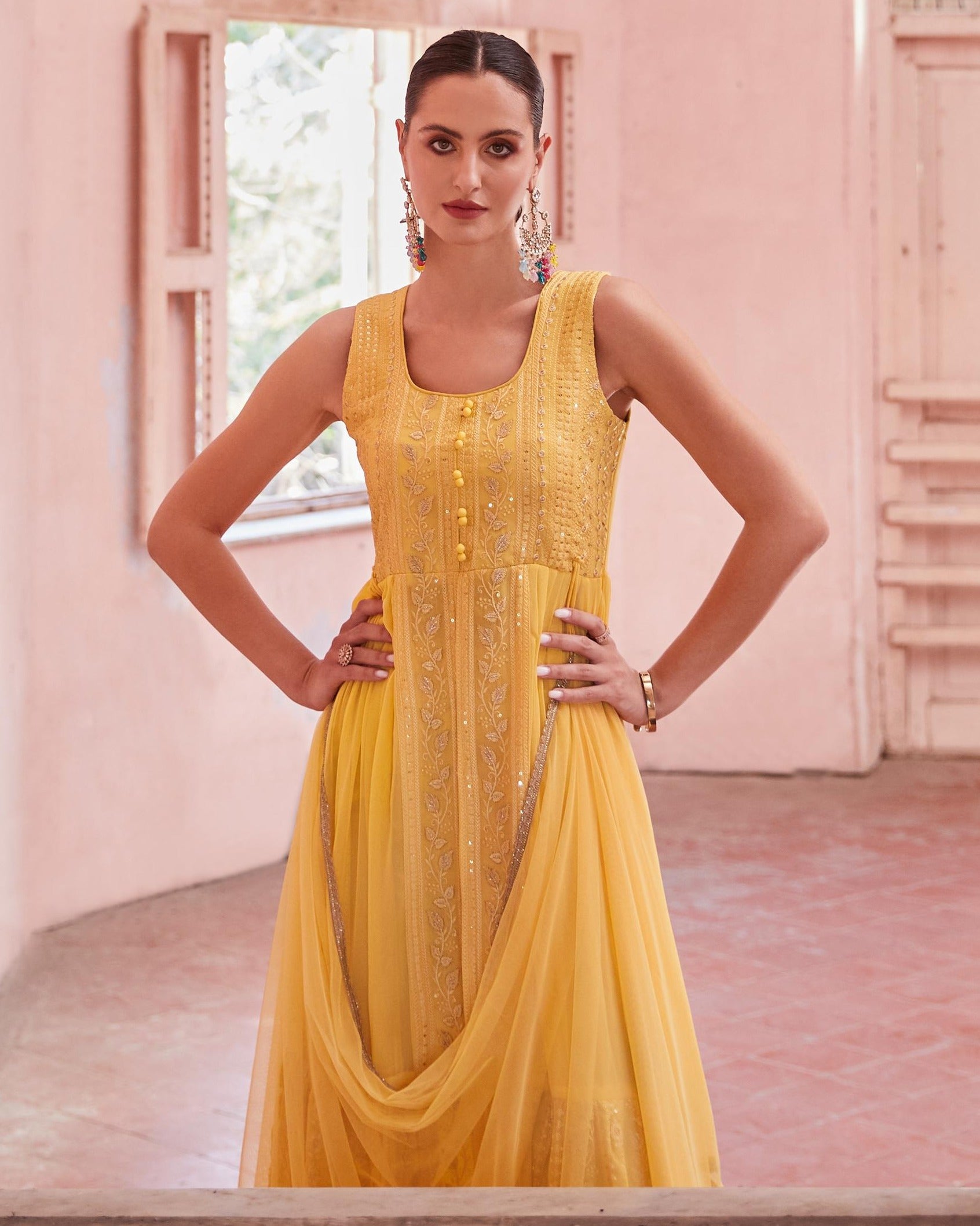Woman wearing a yellow dress with intricate detailing in a softly lit room.