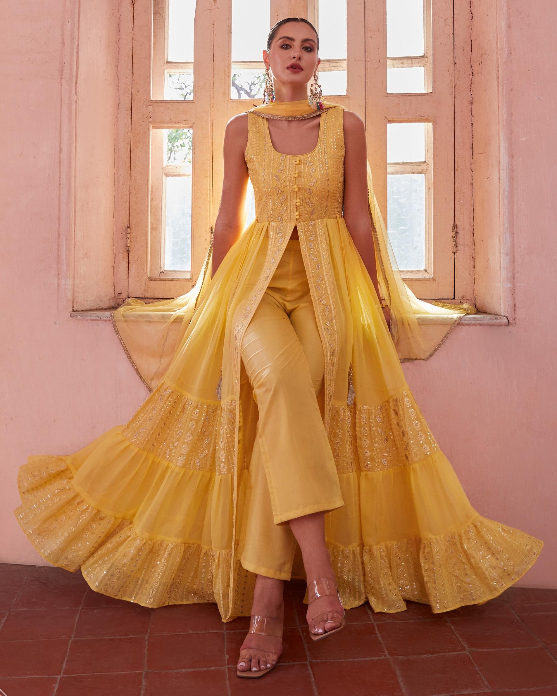 Woman in a yellow outfit standing in front of a window with pink walls.