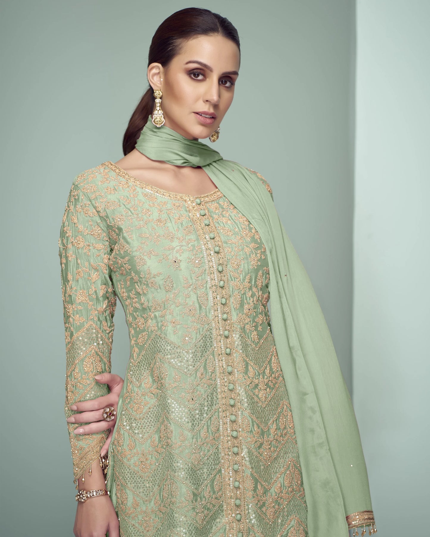 Woman wearing a light green embroidered dress with a matching dupatta against a gray background