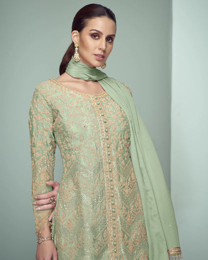 Woman wearing a light green embroidered dress with a matching dupatta against a gray background