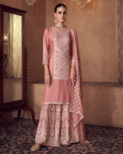 Woman in a traditional pink embroidered outfit standing in an ornate room.