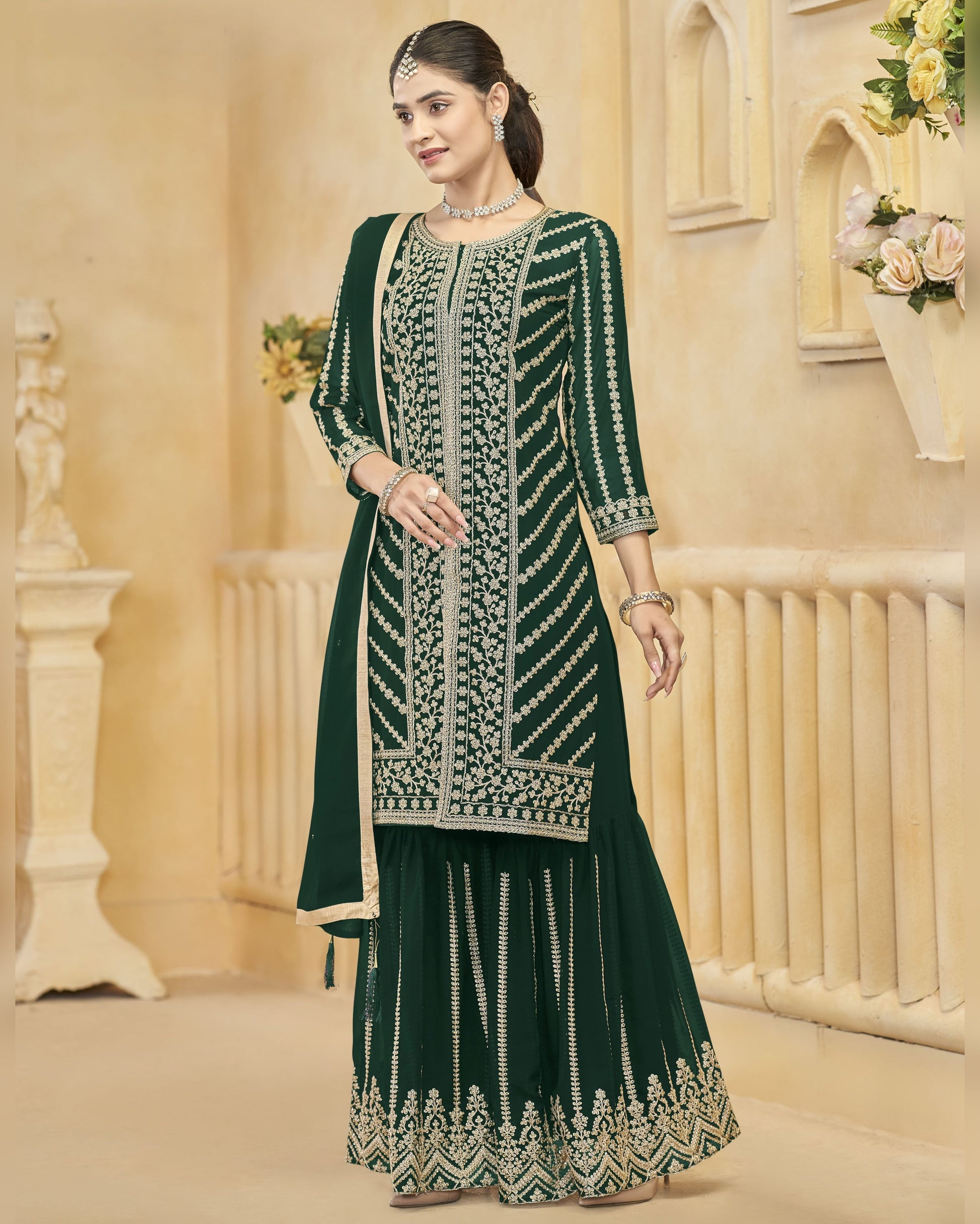 Woman wearing a green embroidered traditional outfit in an elegant indoor setting.