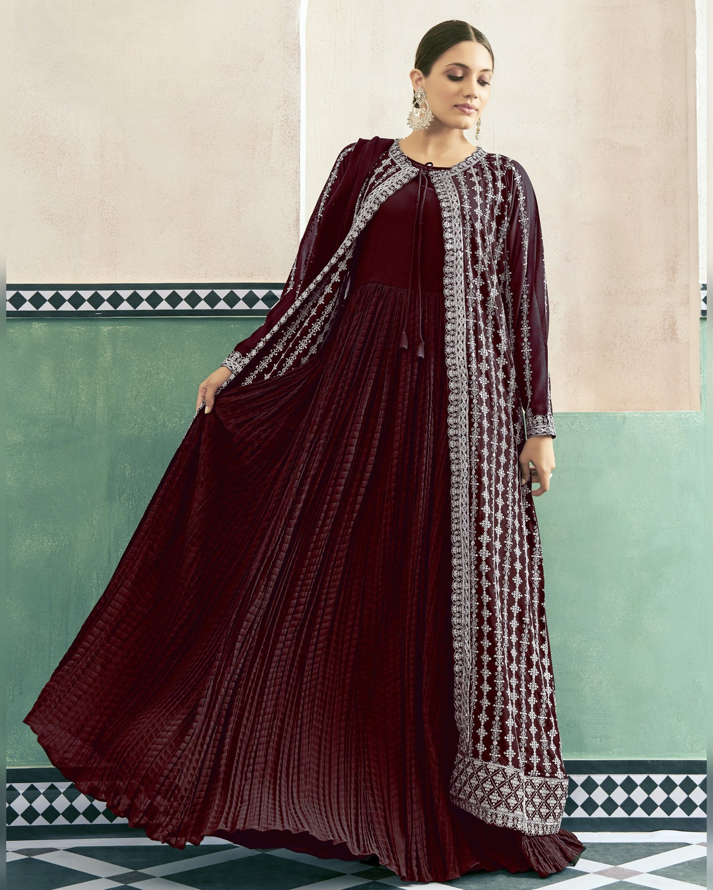 Woman wearing a maroon traditional outfit with intricate patterns in a decorated room.