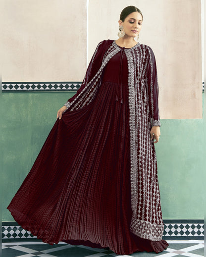Woman wearing a maroon traditional outfit with intricate patterns in a decorated room.