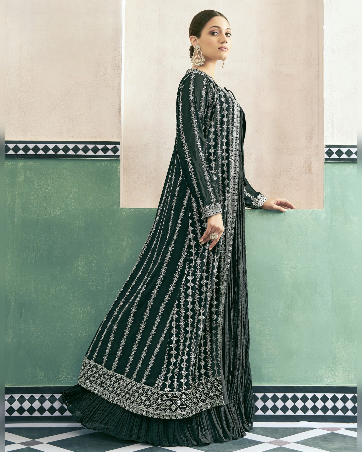 Woman wearing a dark green and silver embroidered traditional outfit in a decorative interior setting.
