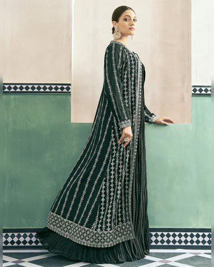 Woman wearing a dark green and silver embroidered traditional outfit in a decorative interior setting.