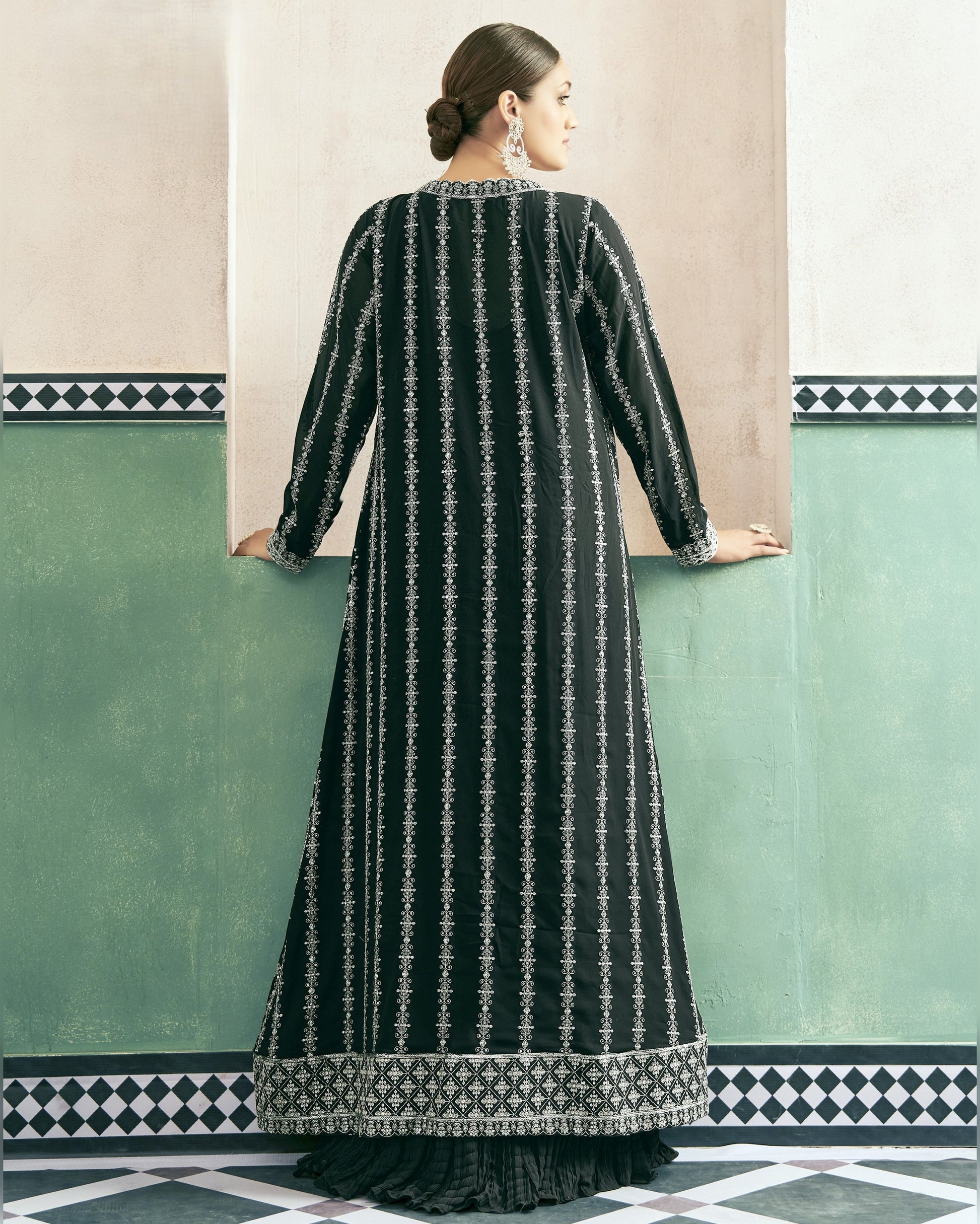 Woman wearing a black and white patterned dress against a green wall with geometric design.