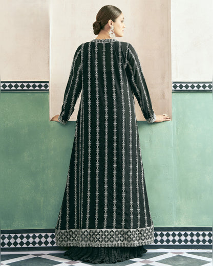 Woman wearing a black and white patterned dress against a green wall with geometric design.