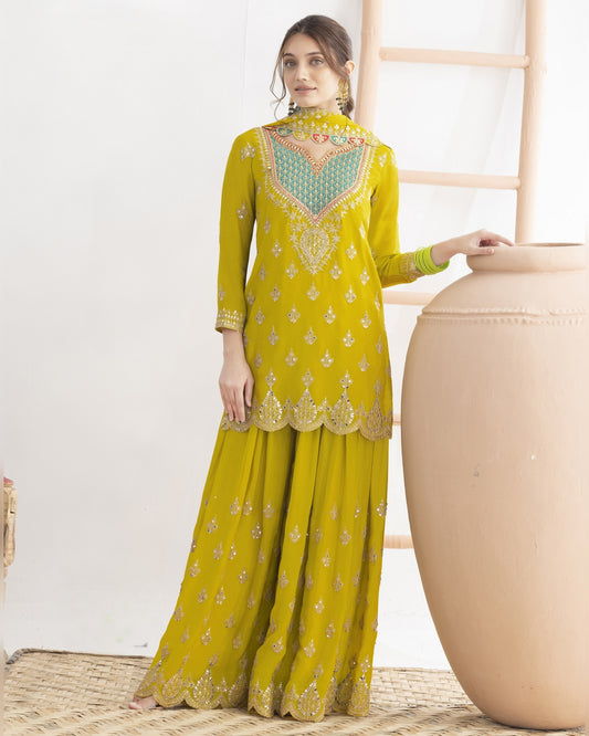 Woman wearing a yellow traditional outfit with green embroidery in a minimalistic setting.