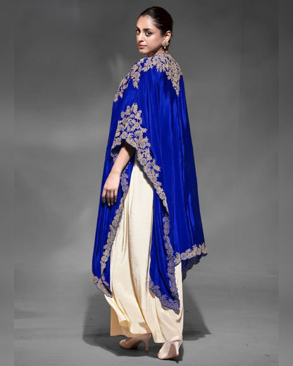 Woman wearing a blue embroidered cape over a cream outfit on a gray background