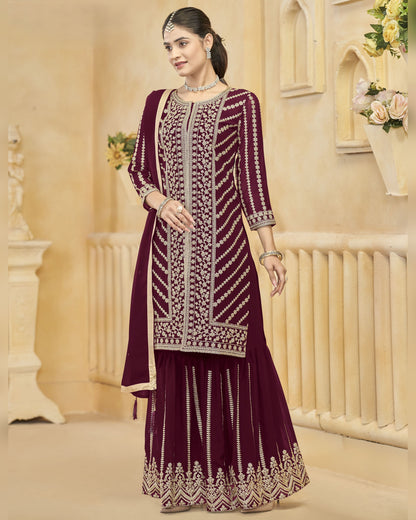 Woman wearing a maroon embroidered traditional outfit in an elegant indoor setting.