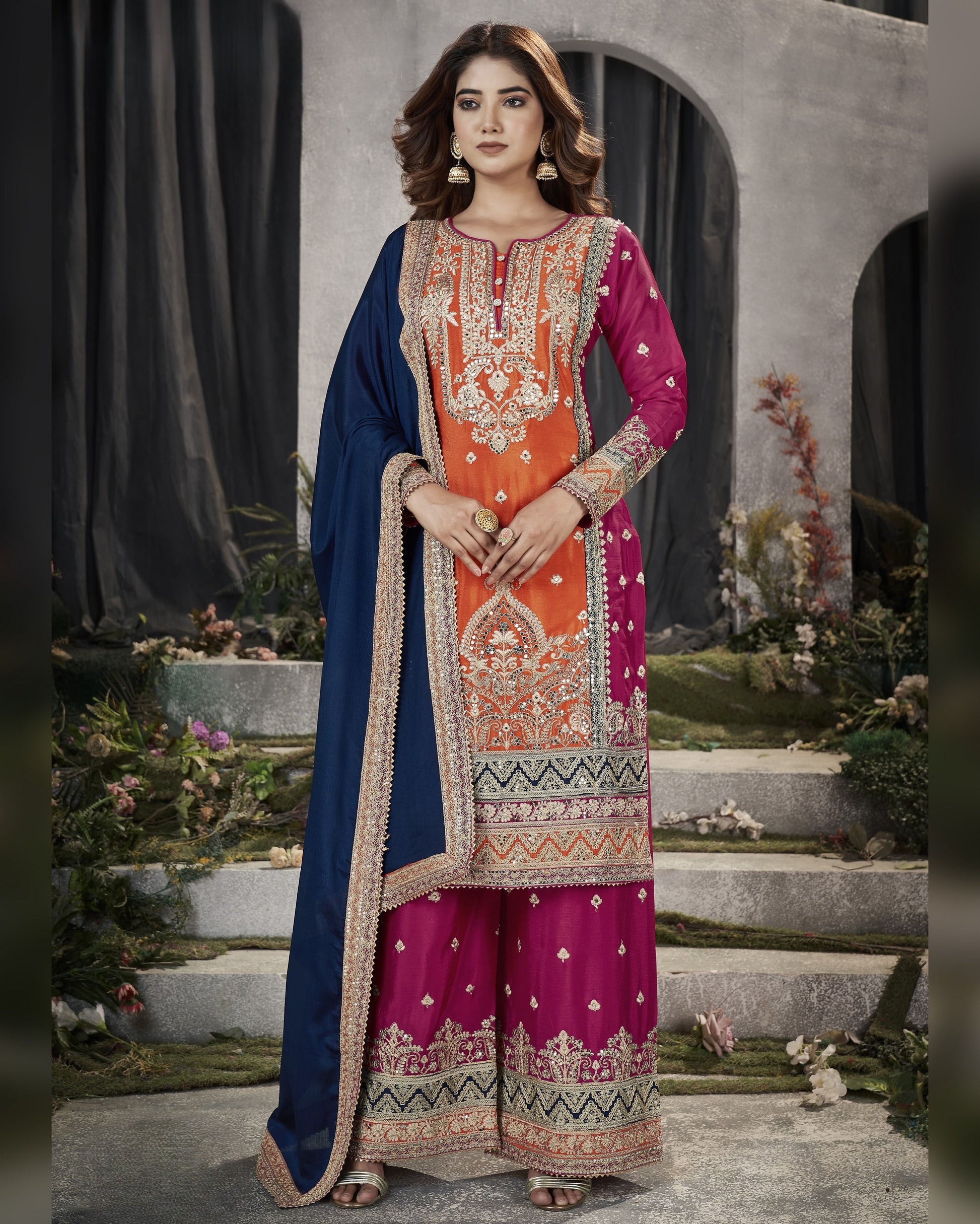 Woman wearing a traditional embroidered outfit with a blue dupatta in an outdoor setting.