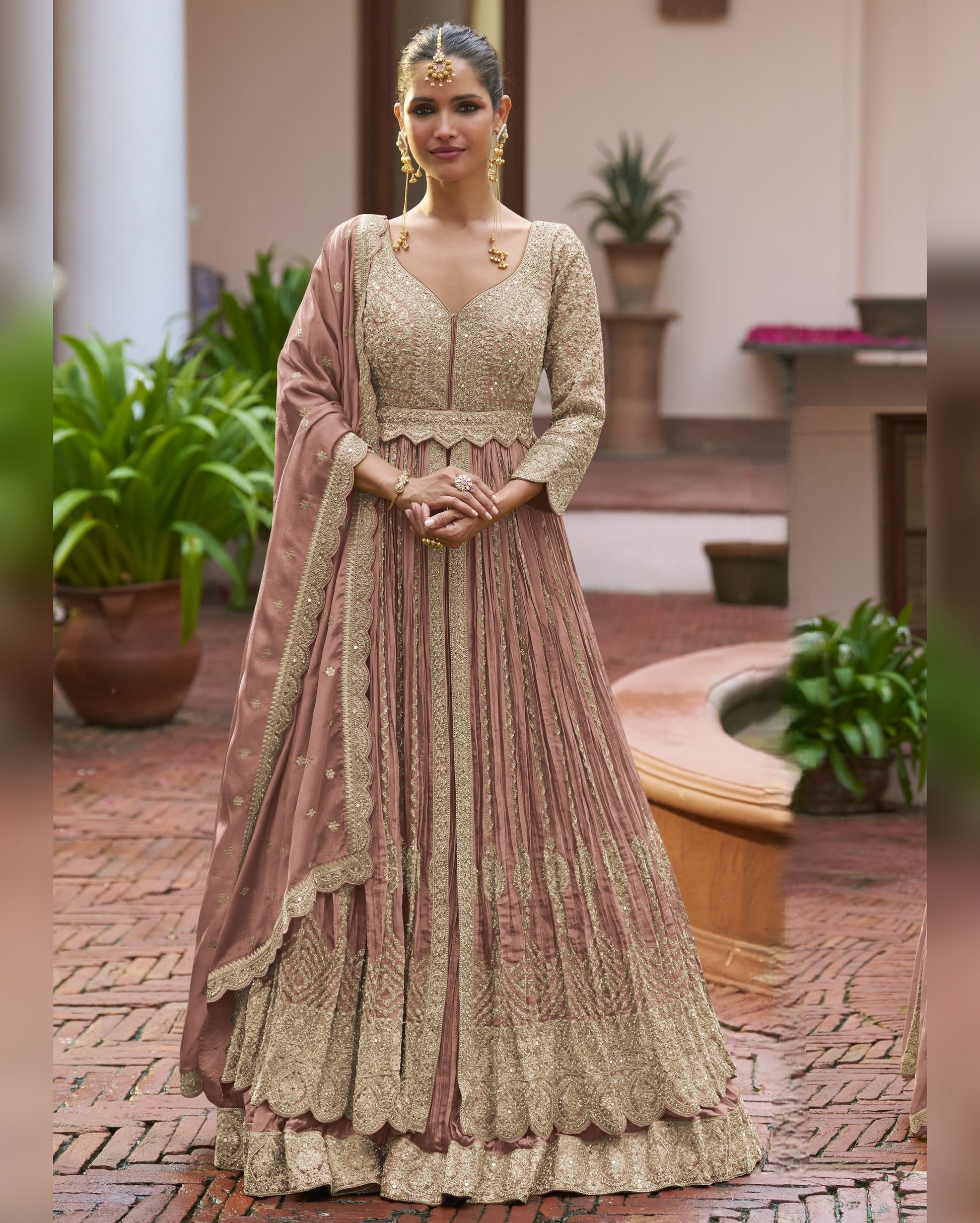 Woman in a traditional outfit standing outdoors with plants and a fountain in the background