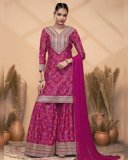 Woman wearing a pink traditional outfit with intricate patterns in a decorative setting.