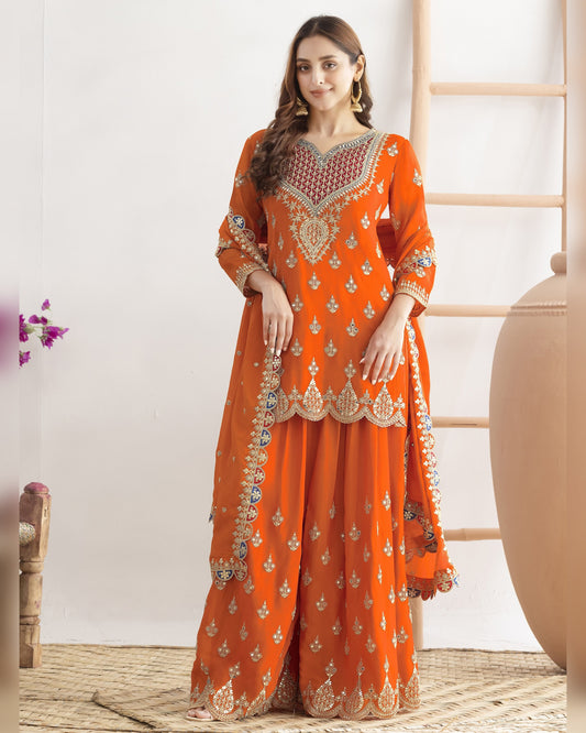 Woman wearing an orange embroidered traditional outfit in a minimalistic setting.