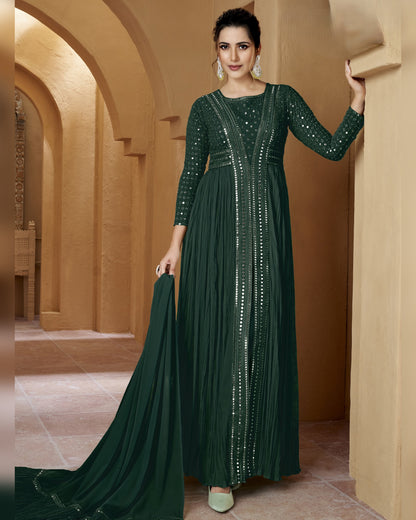 Woman in a dark green dress with sequin details standing in a beige architectural setting.