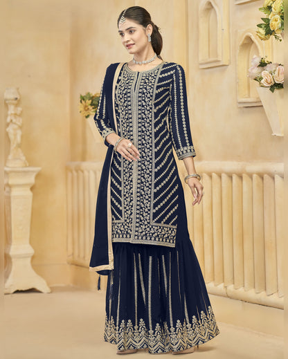 Woman wearing a navy blue embroidered traditional outfit in an elegant indoor setting.